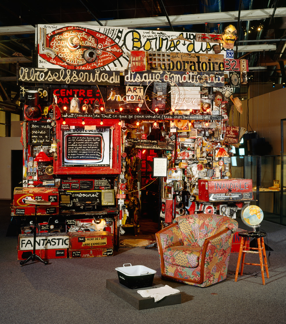 Le Magasin de Ben : un amoncellement d'objets, d'enseignes peintes et d'inscriptions, avec un fauteuil et un globe au premier plan.