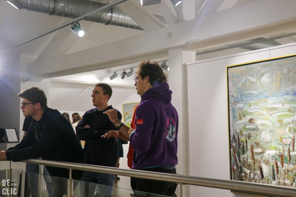 Des visiteurs regardent des tableaux accrochés dans une salle blanche du musée, sous une charpente métallique claire.