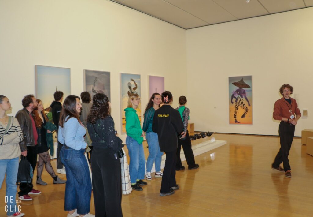 Des visiteurs longent une enfilade de tableaux dans une salle d'exposition lumineuse.
